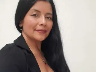 Smiling woman with long black hair wearing a black blouse and silver necklace against a white background.