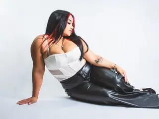 DisyamilPineda poses sitting down in a white bra and black leather pants against a white background.