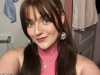 DitzyLilDaisy smiles while wearing a pink halter top, showing her long brown hair with bangs and silver earrings.