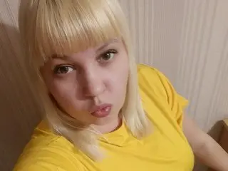 Djessika poses close-up wearing a yellow t-shirt, showing her blonde hair with blunt bangs and a pouty expression.