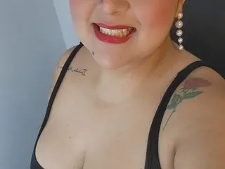 Dulce_mariana smiles while showing her cleavage and chest in a black tank top, showing a tattoo on her shoulder.