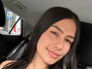 DulcemiaWalk poses with a soft smile, showing her long dark hair and clear skin while looking directly at the camera in a car setting.