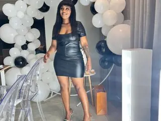 EbonyBentley poses in a black leather dress, showing off her hair and legs in a bright room with white balloons.