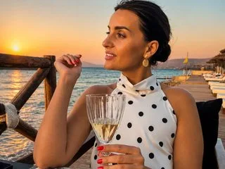 EdithQuillian smiles while holding a glass of white wine on a balcony overlooking the ocean at sunset.