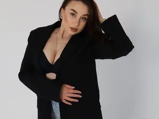 ElisSton1009 poses in a black blazer with a deep neckline, showing her cleavage and long dark hair against a plain white background.
