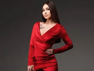 ElisaVel poses in a tight red dress, showing off her long dark hair and chest tattoo against a dark background.