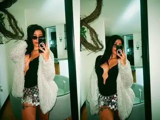 ElizabetthMacy poses for a mirror selfie wearing a black top and a white fuzzy cardigan, showing her long dark hair and sunglasses.