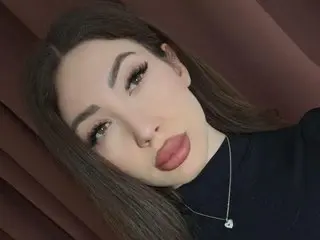 ElleLuvv poses close-up with long brown hair and a dark turtleneck, looking directly at the camera with a pouty expression.