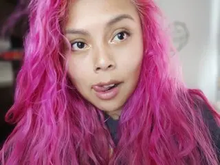 EllieAutumn shows her long, wavy pink hair and direct gaze while looking toward the camera in a close-up shot.