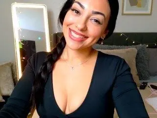 EllieKae smiles while wearing a black long-sleeved top, showing her dark hair styled in a long braid over her shoulder.