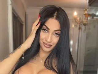 EmaHallee poses with her long black hair, running her hand through it while looking at the camera with a smile.