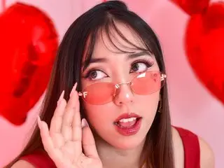 Emi_Star looks at the camera with a pouty expression, showing her long dark hair and wearing red-tinted sunglasses against a pink background.