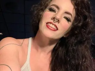 EmieXO poses with her long, curly dark hair, showing her face, neck, and chest while wearing a white tank top top.