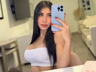 EmilyDuque poses for a mirror selfie, showing her long dark hair and white tube top while looking directly at the camera.