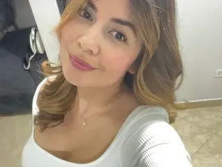 Smiling young woman in a white ribbed top posing for a bright indoor selfie.