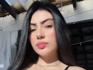 Young woman with long dark hair and soft makeup posing outdoors in natural sunlight.