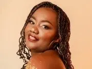 EmmaBrantt poses with a smile, showing her dark hair in long braids and her bare shoulders against a plain background.