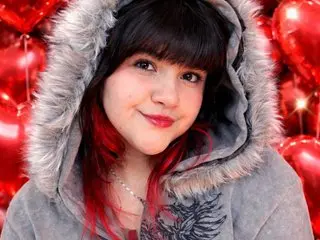EmmaLush smiles while wearing a grey hooded sweatshirt with thick, light grey faux fur lining the hood, her dark hair visible underneath.
