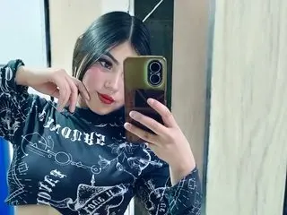 EmmadZack poses for a mirror selfie wearing a black long-sleeve patterned top, showing her dark hair and red lipstick.