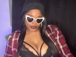 EmpressPhoenix wears heart-shaped sunglasses and a red plaid shirt, showing cleavage in a black lace bra while looking at the camera.