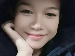EnaQueen smiling at the camera while resting her chin on her hand.