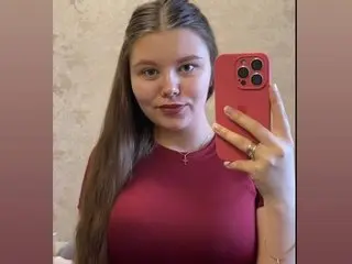 Enchaantress poses for a selfie, wearing a maroon top with her long brown hair styled straight down against a neutral wall.