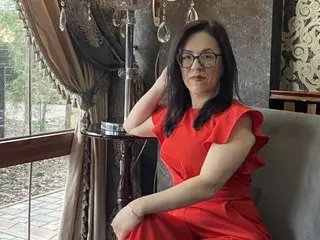 Elegant woman in a red dress sitting by a window in a sophisticated, moody interior setting.
