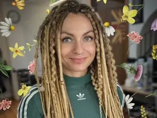 Smiling woman with long blonde dreadlocks wearing a green Adidas shirt amidst a colorful floral overlay.