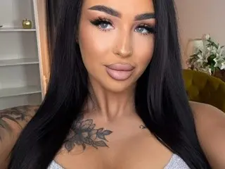 EvaXRoseX with long black hair, wearing a light purple top, looking directly at the camera in a close-up shot.