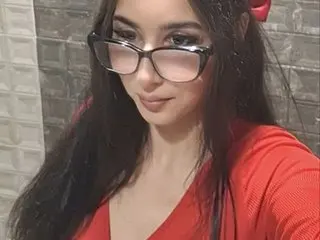 Young woman with long dark hair and glasses wearing a red top in a modern indoor setting.