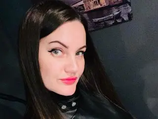 EvelynCalli looks into the camera with long dark hair and pink lipstick, wearing a black leather top.