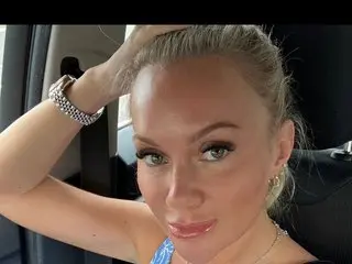 Eviebaby95 poses with her hands behind her head, showing her blonde hair and light eyes in a close-up shot.