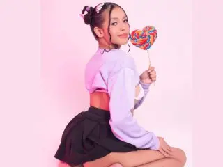 EvonieCarter poses in a light purple long-sleeve top and black skirt, holding a large rainbow lollipop against a plain pink background.
