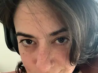 EyesUpHere shows her face and dark hair while wearing black headphones in a close-up selfie.