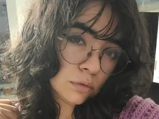 Faekitten97 with messy dark hair, wearing a purple knit top and looking directly at the camera.
