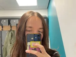 Floraexploration takes a mirror selfie, showing her long brown hair and face while holding her phone up to her mouth.