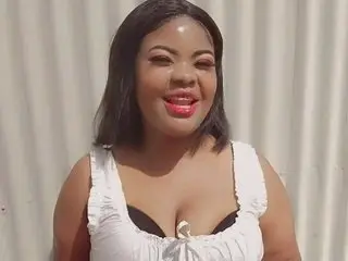 FlowerSaltry poses in a white lace-up top, showing her cleavage and dark hair against a light neutral background.