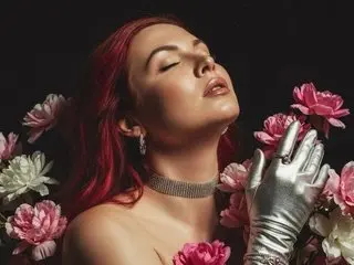 Foxy28 poses with her eyes closed, wearing a silver choker and silver gloves against a dark background.