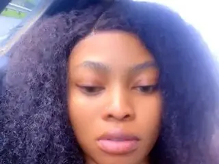 FreakyNancy100 looks directly at the camera with her dark, voluminous curly hair framing her face.