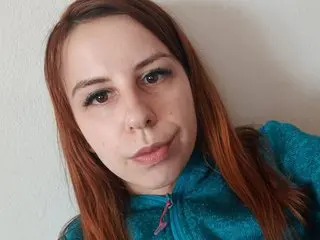 Redheaded woman in a teal fleece sweater smiling softly against a neutral wall.