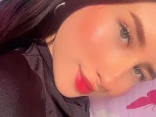GabbieBenso poses close-up with a soft smile, showing her face, eyes, and red lips against a dark background.