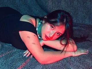 Gabbycooper poses with her arms crossed, showing her bare shoulders and cleavage while looking at the camera with long dark hair.