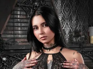 GabyMathewss poses with long black hair, wearing a black lace choker and a black lace top that shows her cleavage and shoulders.