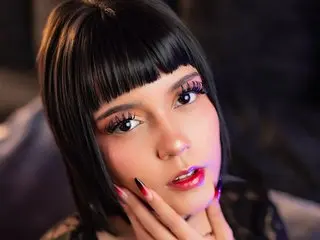 Young woman with black bangs and dramatic eye makeup posing in a moody, dark setting.