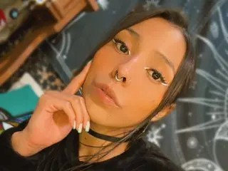 Young woman with nose ring and black choker posing in a moody, celestial-themed room.