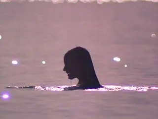 Silhouette of a woman swimming in the ocean during a dreamy pink sunset.