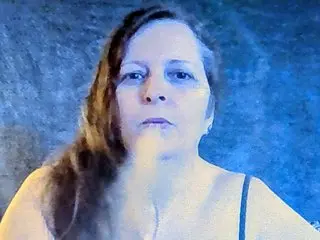 GemmaGibbs shows her face and long dark hair against a blue background, wearing a black strap top.