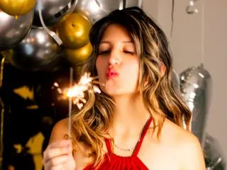 GiaRoussel21 poses with long wavy hair, blowing a kiss while holding a lit sparkler in a dark setting with gold balloons.