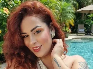 GiannaJohns smiles by a swimming pool with her red hair flowing over her shoulder.