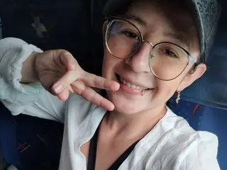 Smiling young woman with glasses and a white shirt making a peace sign in a casual indoor setting.
